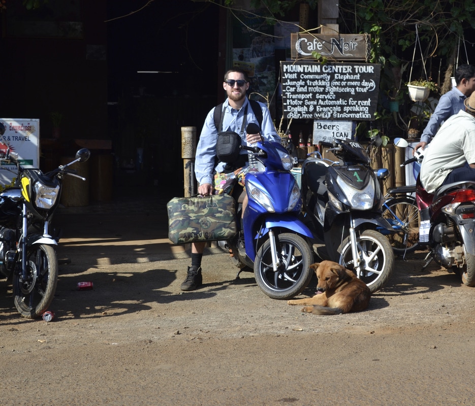 Traveler with luggage beside a blue scooter outside a local café